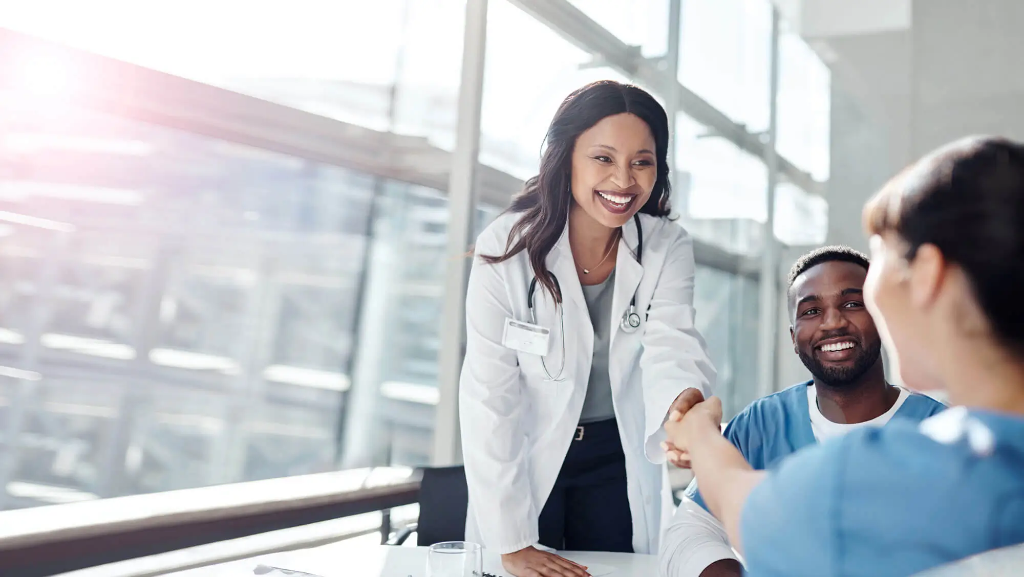 Friendly woman doctor with nurse, shaking hands with another person
